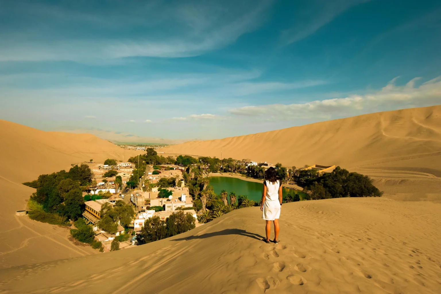 Woman standing on Huacachina sand dunes overlooking Huacachina Oasis lagoon in Ica Peru - Paracas to Huacachina Bus - Wayki Bus
