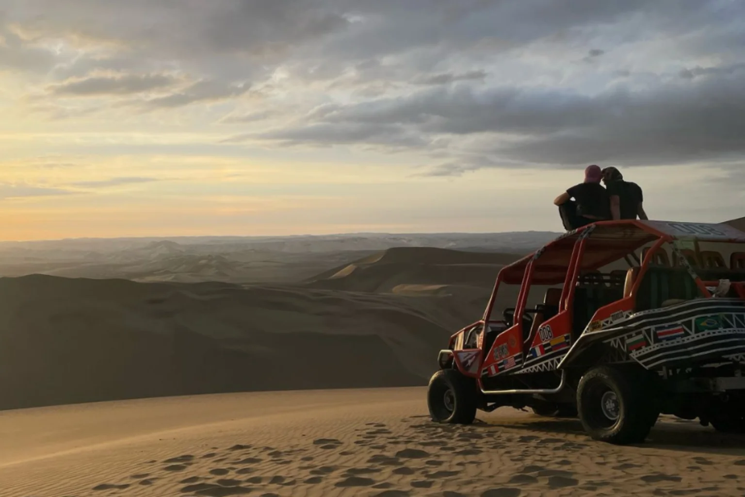 Couple of travelers enjoying the sunset after the Dune buggy and sandboarding tour in Huacachina - Wayki Bus